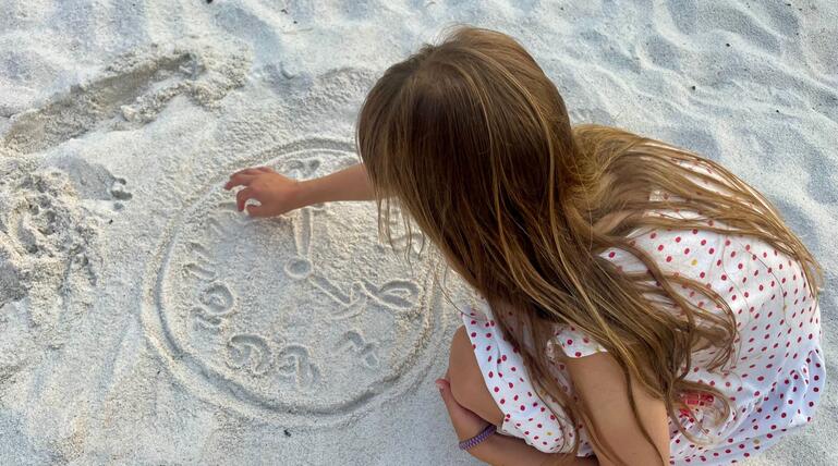 Kind malt eine Uhr in den Sand