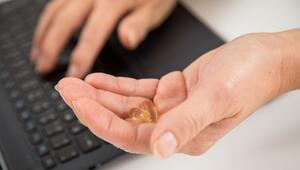 Eine Frau sitzt am Laptop und hält Kapseln in der Hand