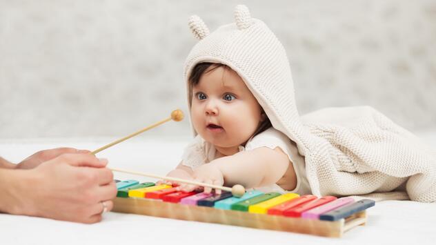 Baby, das am Glockenspiel sitzt und Mutter zusieht. 