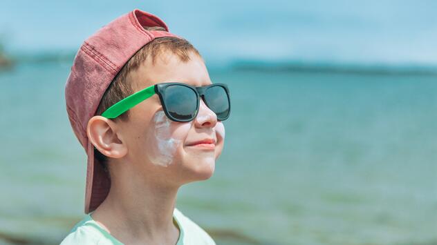 Junge am Strad mit Sonnencreme im Gesicht