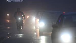 Fahrräder und Autos fahren am Morgen durch den Nebel.