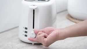 Eine Hand dreht an dem Regler eines weißen Toasters.