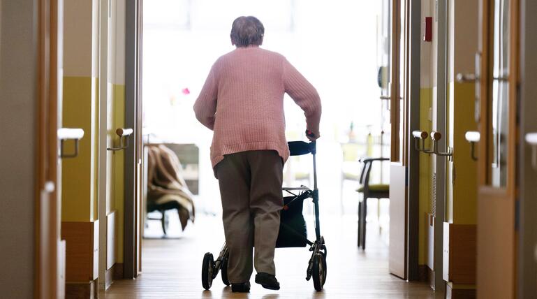 Eine Frau geht mit einem Rollator in einem Altenheim