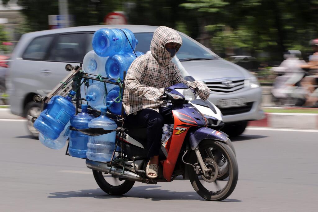 Mann fährt in Vietnam Kanister mit Wasser auf dem Roller. Er schützt sich mit langen Sachen.