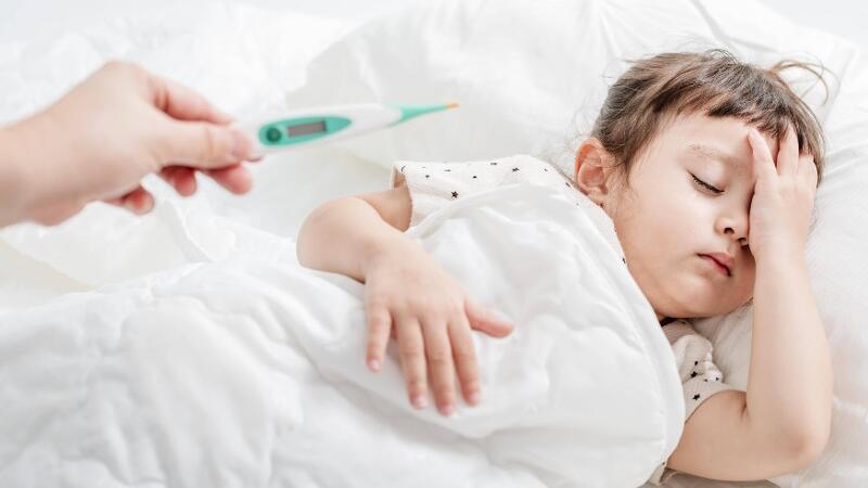 Ein kleiner Junge liegt krank im Bett mit Fieber.