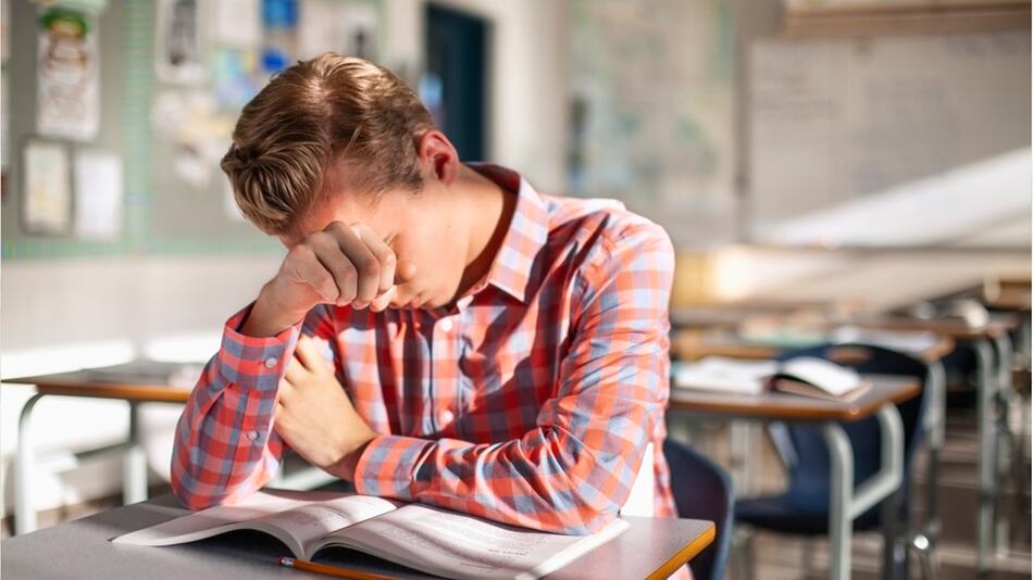 Ein Schüler sitzt einsam im Klassenzimmer und verzweifelt