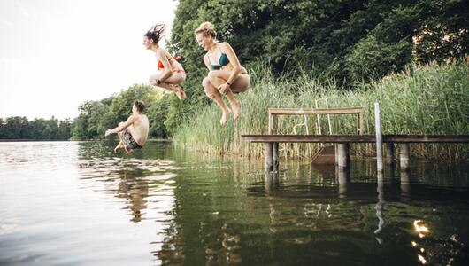 Drei junge Menschen springen in einen See