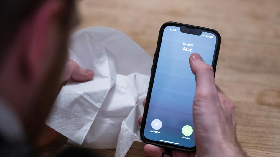 Mann hält Taschentuch und ein Telefon mit dem Schriftzug "Arzt"
