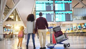 Eine Familie steht in einem Flughafen vor der Anzeigetafel.