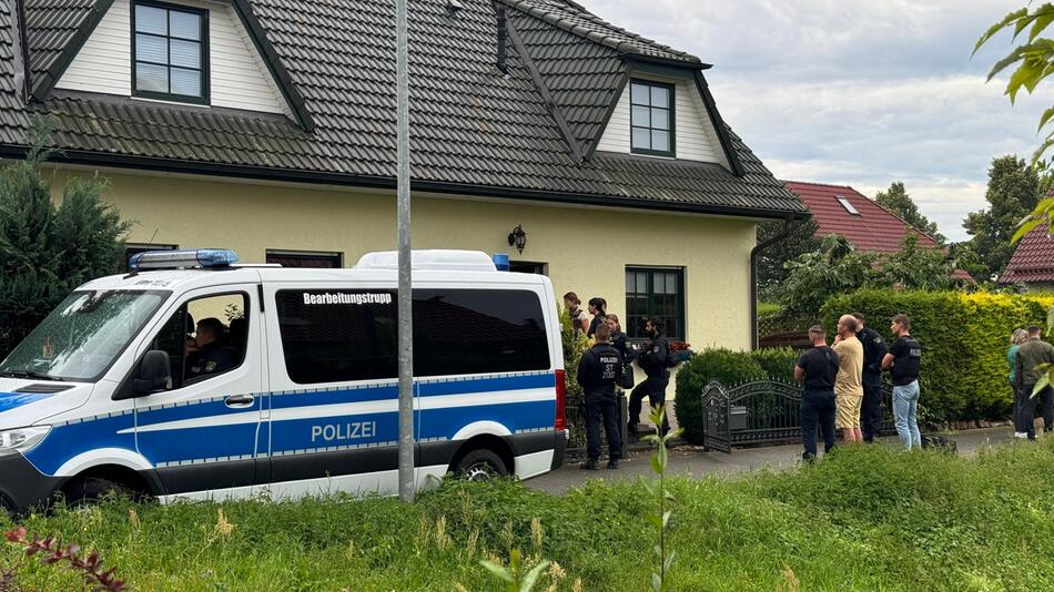 Polizisten stehen vor einem Einfamilienhaus auf der Straße.