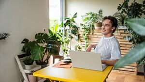 Mann sitzt zwischen Pflanzen an seinem Laptop im Homeoffice
