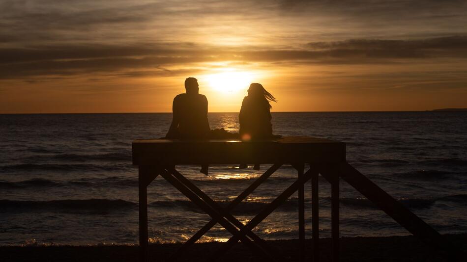 Paar sitzt bei Sonnenuntergang am Strand von Arenal