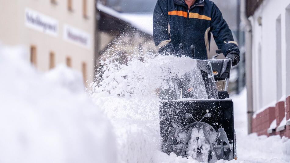 Ein Mann beräumt den Gehweg mit einer Schneefräse