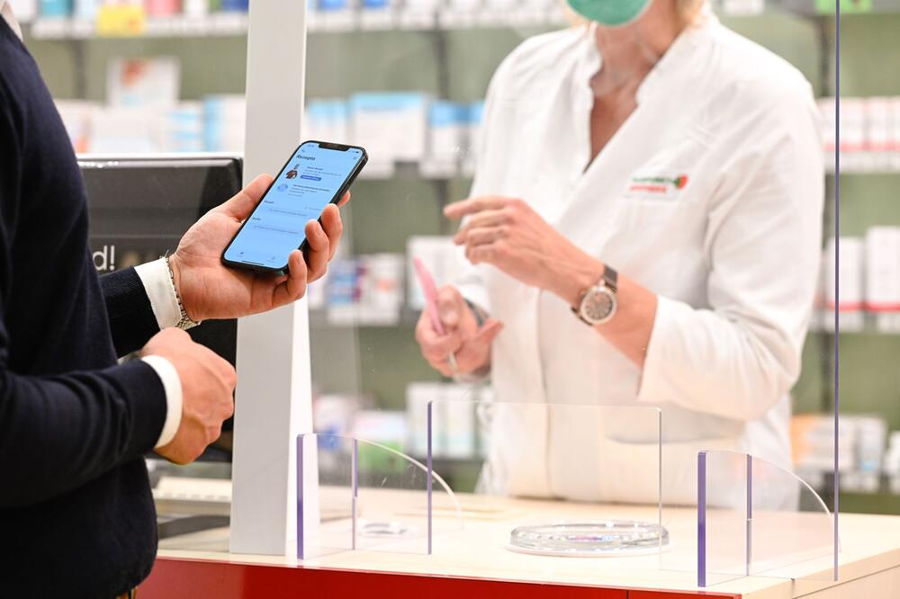 Mann zeigt auf einem Smartphone ein E-Rezept in einer Apotheke