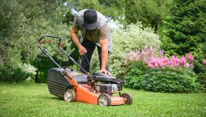 Ein erwachsener Mann startet im Garten seinen Rasenmäher.