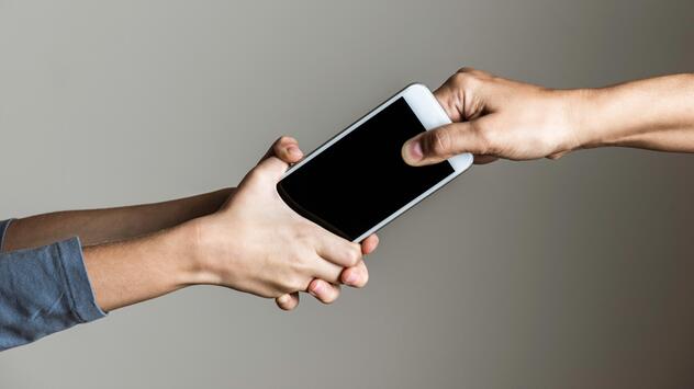 Kind klammert sich an ein Smartphone, das eine erwachsene Person aus der Hand nehmen möchte