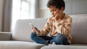 Kleines Kind sitzt auf Sofa und blickt gelangweilt ins Handy