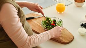 Eine schwangere Frau isst einen frischen Salat mit Spinat und Tomaten aus einer Glasschüssel ...