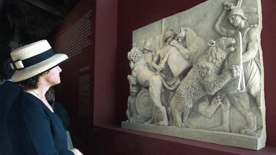 Eine Journalistin betrachtet ein antikes Relief mit der Darstellung von Gladiatorenkämpfen