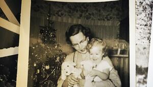 Altes Polaroid einer Mutter, die ein Kind auf dem Arm hält, dahinter ein Weihnachtsbaum. 