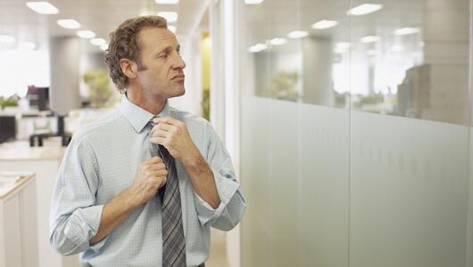 Mann richtet mit arrogantem Blick seine Krawatte im Büro