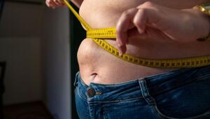 Eine Frau mit Übergewicht hält ein Maßband um ihren Bauch.
