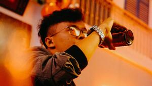 Junger Mann mit Brille und silberner Armbanduhr trinkt aus einer braunen Glasflasche ...