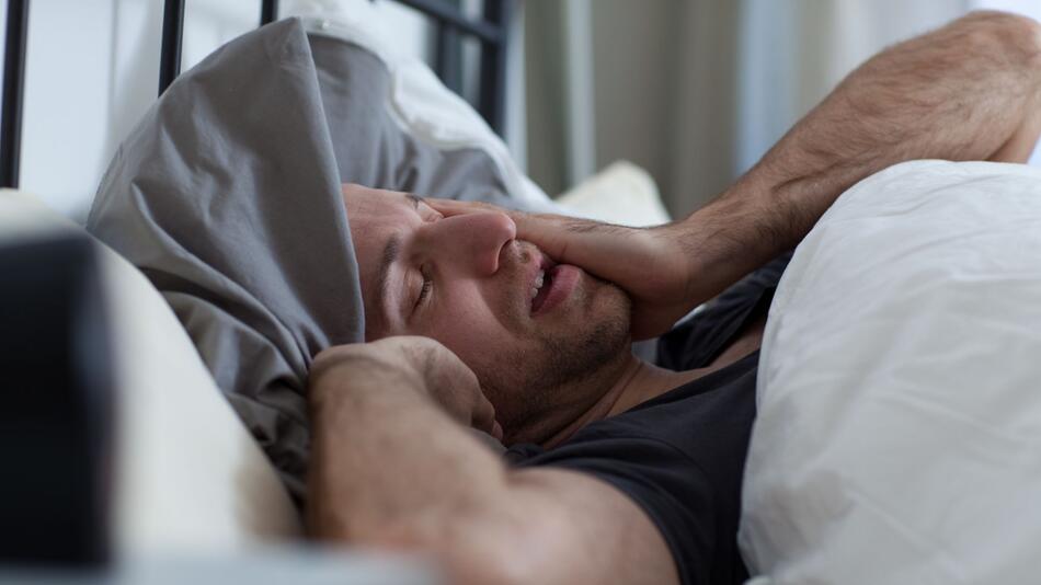 Ein Mann reibt sich die Augen im Bett