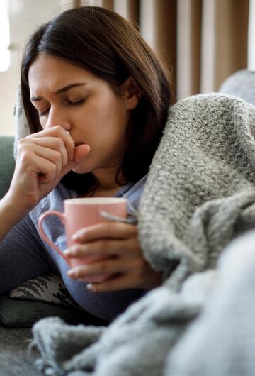 Frau ist erkältet, trinkt Tee, hustet und liegt auf dem Sofa