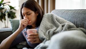 Frau ist erkältet, trinkt Tee, hustet und liegt auf dem Sofa