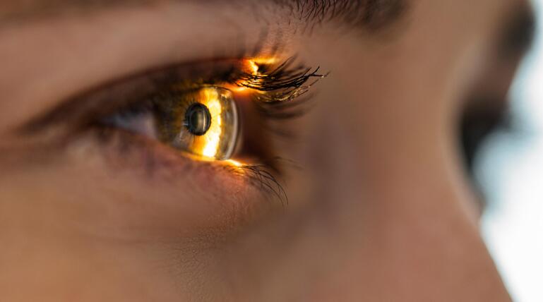 Auge in Nahaufnahme, ein Lichtschein fällt auf die Iris