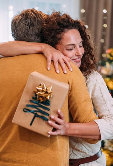 Frau umarmt einen Mann dankbar mit Geschenk in der Hand