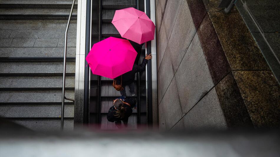 Symbolbild: Personen mit Regenschirmen nutzen Rolltreppe, von oben fotografiert