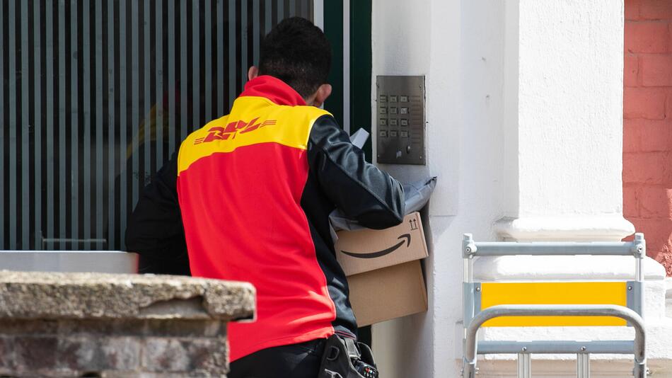Postbote der DHL steht vor einer Haustür