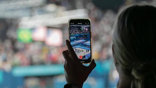 Ein weiblicher Fan filmt die Siegerehrung im Turnen der Frauen von der Tribüne aus mit