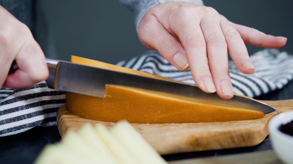 Eine Frau schneidet die Rinde von einem Stück Käse ab.