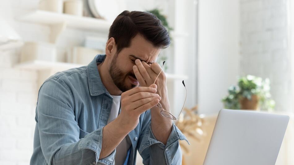 Man reibt sich am PC die Augen, Brille in der Hand