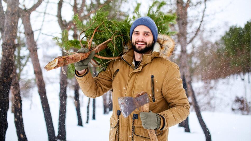 Ein Mann schlägt seinen Weihnachtsbaum im Wald.
