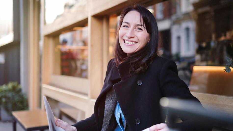 Eine Frau sitzt mit einer Zeitung vor einem Gebäude