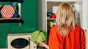 Eine Frau hält einen Kohl vor einem offenen Kühlschrank
