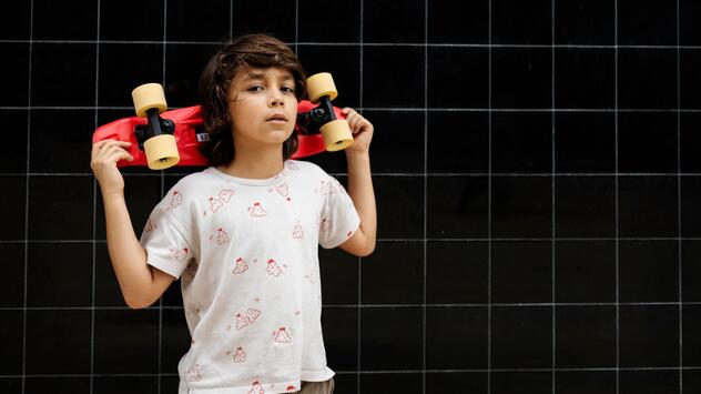 Selbstbewußter Junge trägt ein Skateboard auf seinen Schultern