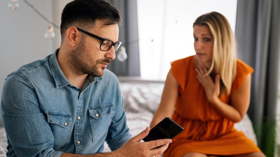 Mann mit Handy und skeptische Frau im Hintergrund