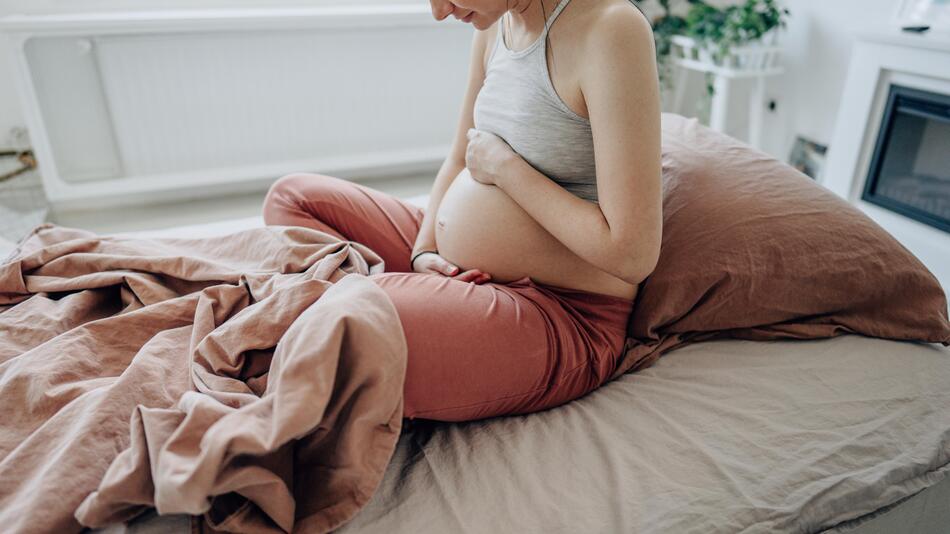 schwangere Frau sitzt auf Bett