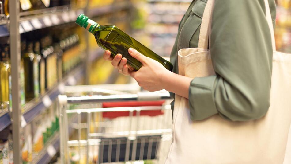 Frau betrachtet Ölivenölflasche im Supermarkt