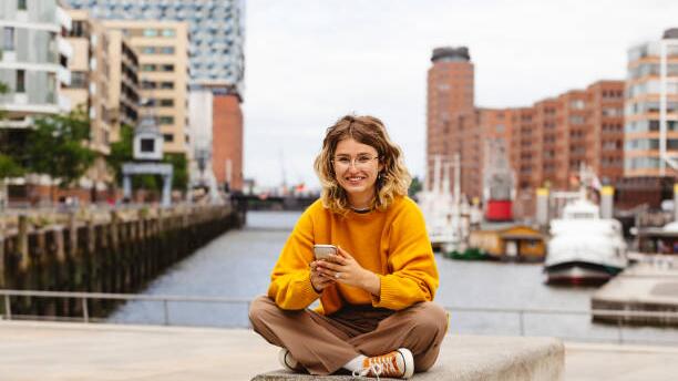 Eine junge Frau sitzt glücklich vor der Elbe in Hamburg.