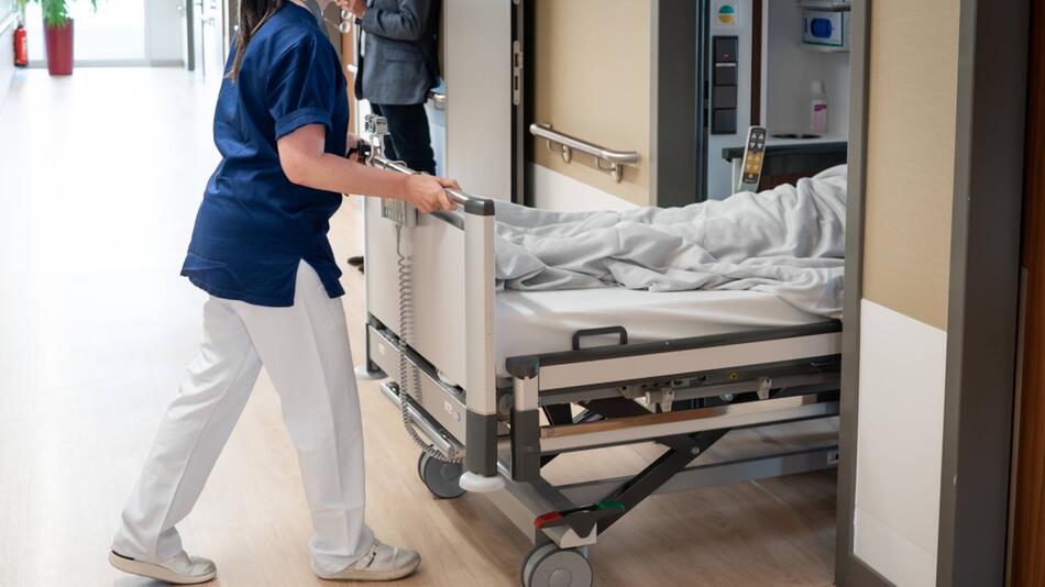 Eine Pflegerin schiebt ein Krankenhausbett in ein Zimmer
