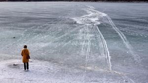 Eine Frau steht am zugefrorenem See nahe einer Einbruchstelle