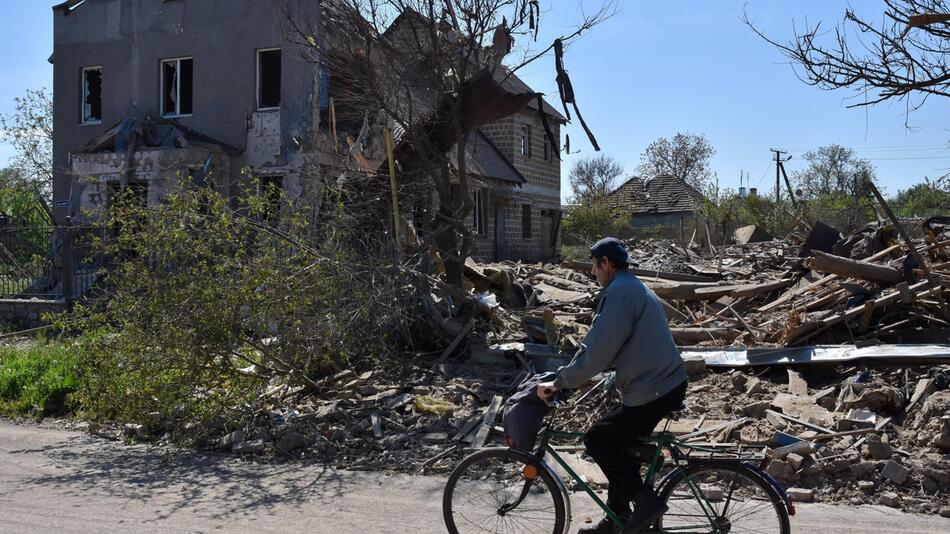 Ein Mann radelt an einem zerstörten Gebäude vorbei.