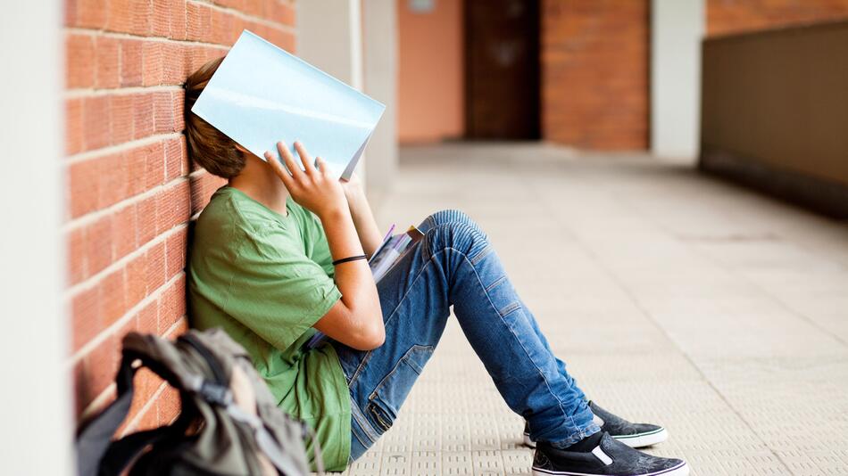 Verzweifelter Schüler sitzt in der Schule, Heft über dem Gesicht, Notendruck