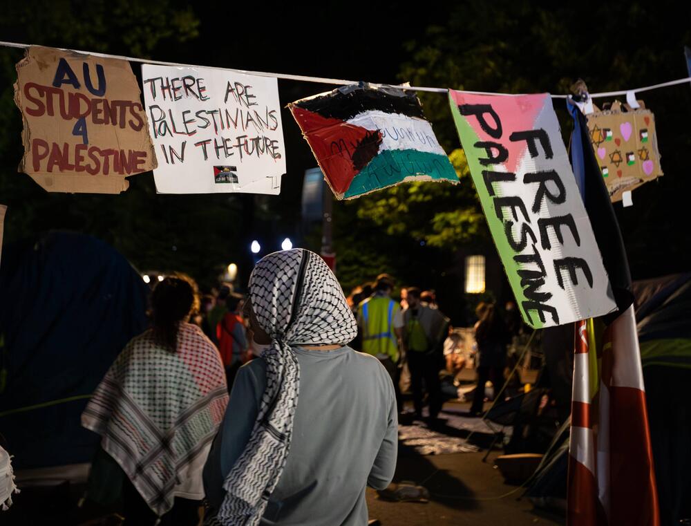 Eine Frau im Kopftuch läuft unter einem "Free Palistine" Schild durch